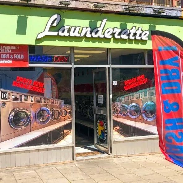 The painted shopfront of New Cross Launderette at 369 New Cross Road, with the trompe l'oeil window showing rows of washing machines.